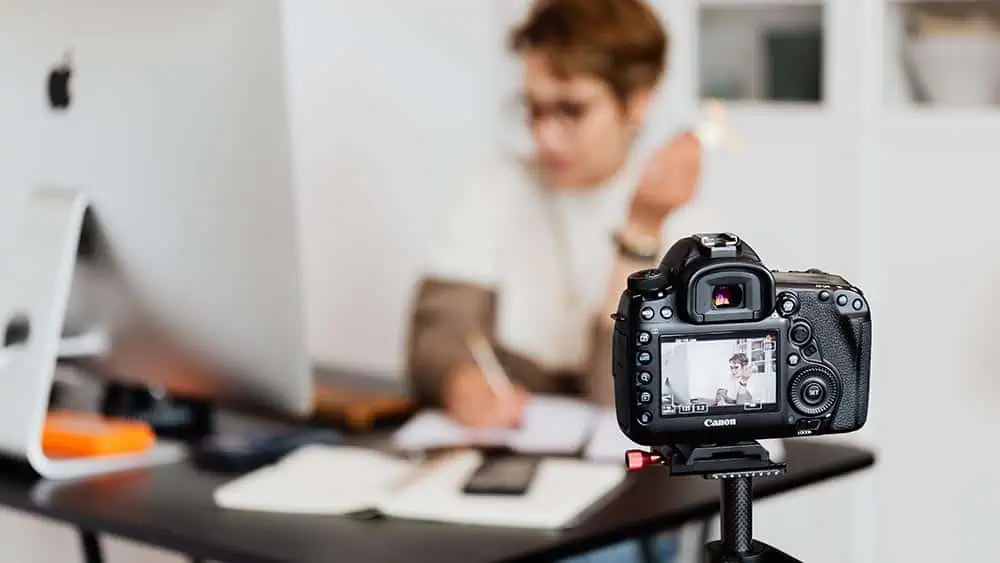 Canon spiegelreflexcamera op statief filmt persoon aan een bureau