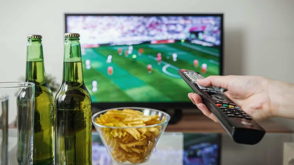 Tv met voetbalwedstrijd achter een bakje chips en twee flesjes bier