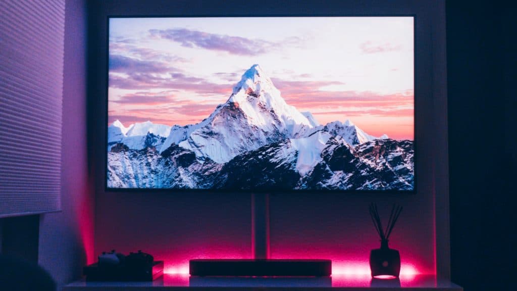 Tv-scherm op muur in donkere kamer met roze lampen eronder