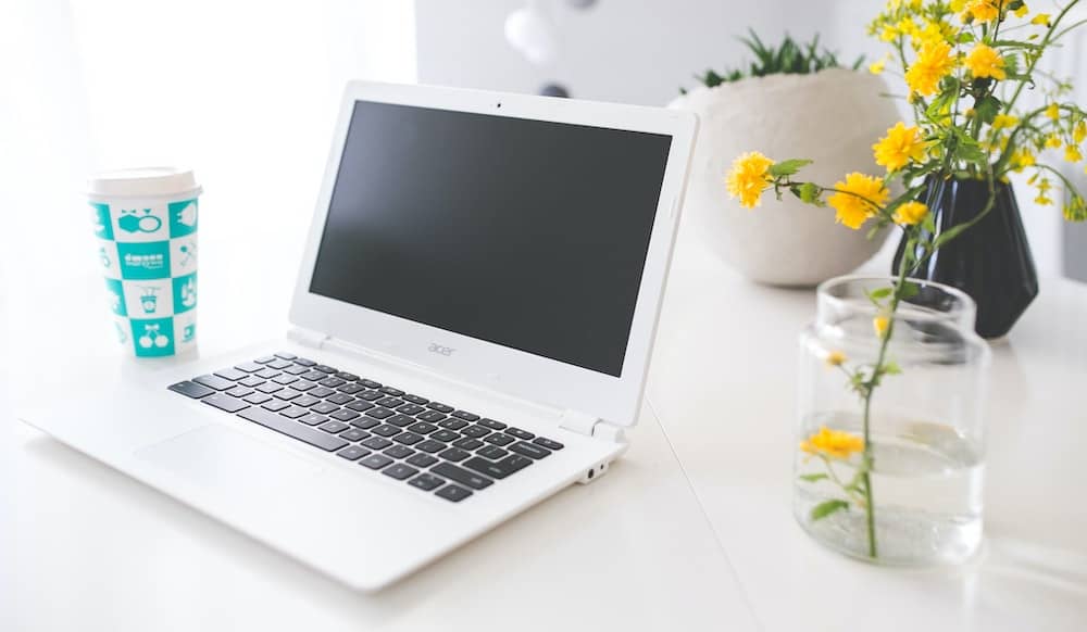 Witte Chromebook op een wit bureau met een gele bloem ernaast