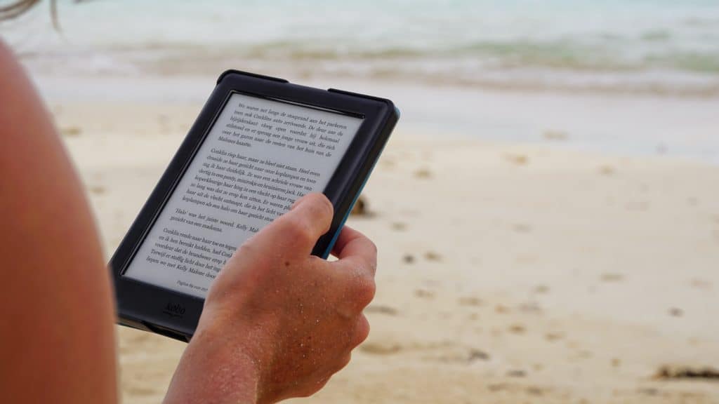 Iemand die met een e-reader op een strand leest