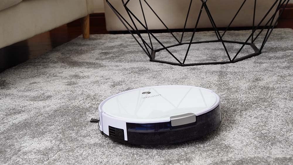 Een witte robotstofzuiger reinigt een grijs tapijt