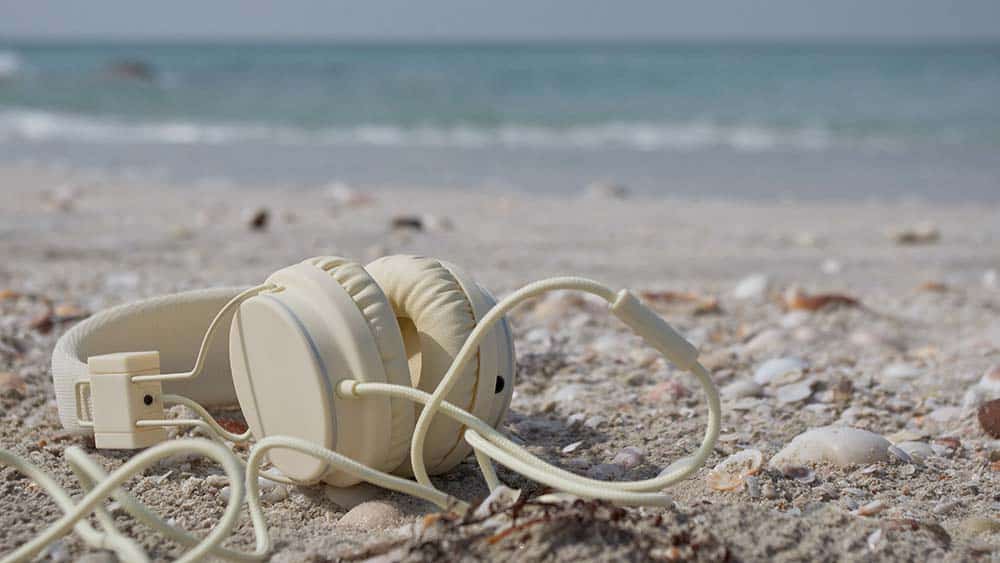 Een beige koptelefoon met snoer ligt op het strand
