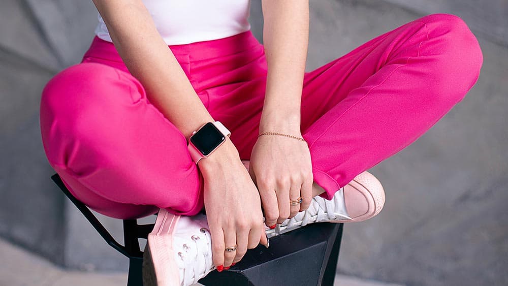 Vrouw zit op een kruk met een roze smartwatch om de pols