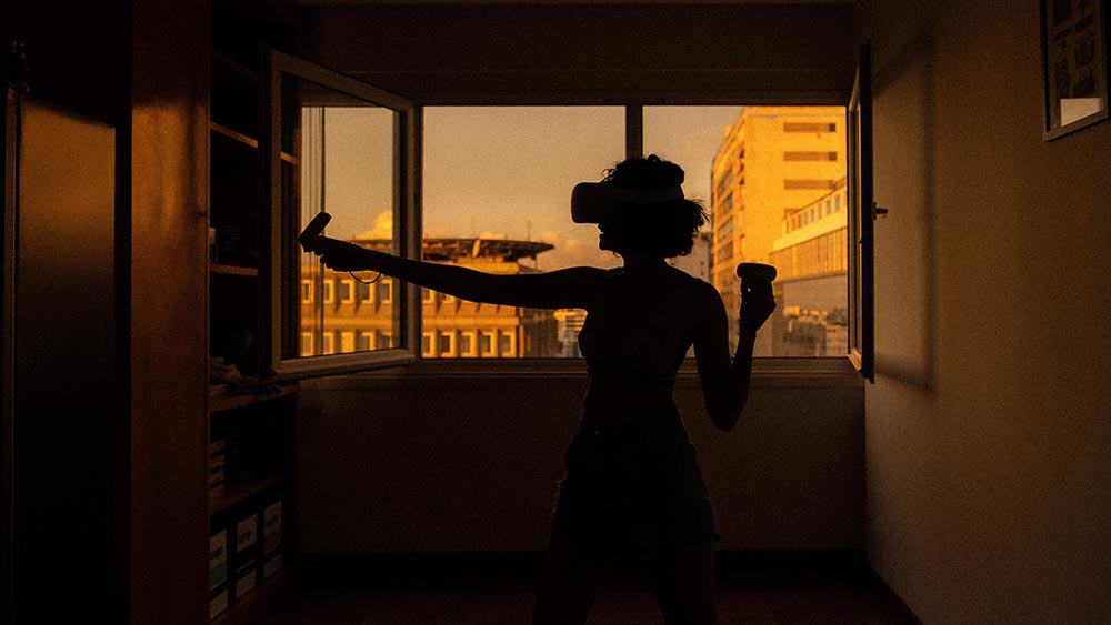 vrouw met vr-bril en controller in een kamer met open raam en zonsondergang