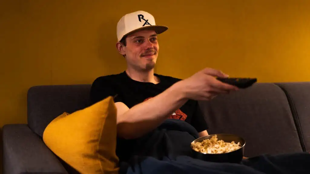 Een jongen die op de bank zit om een film te gaan kijken met een bak popcorn.