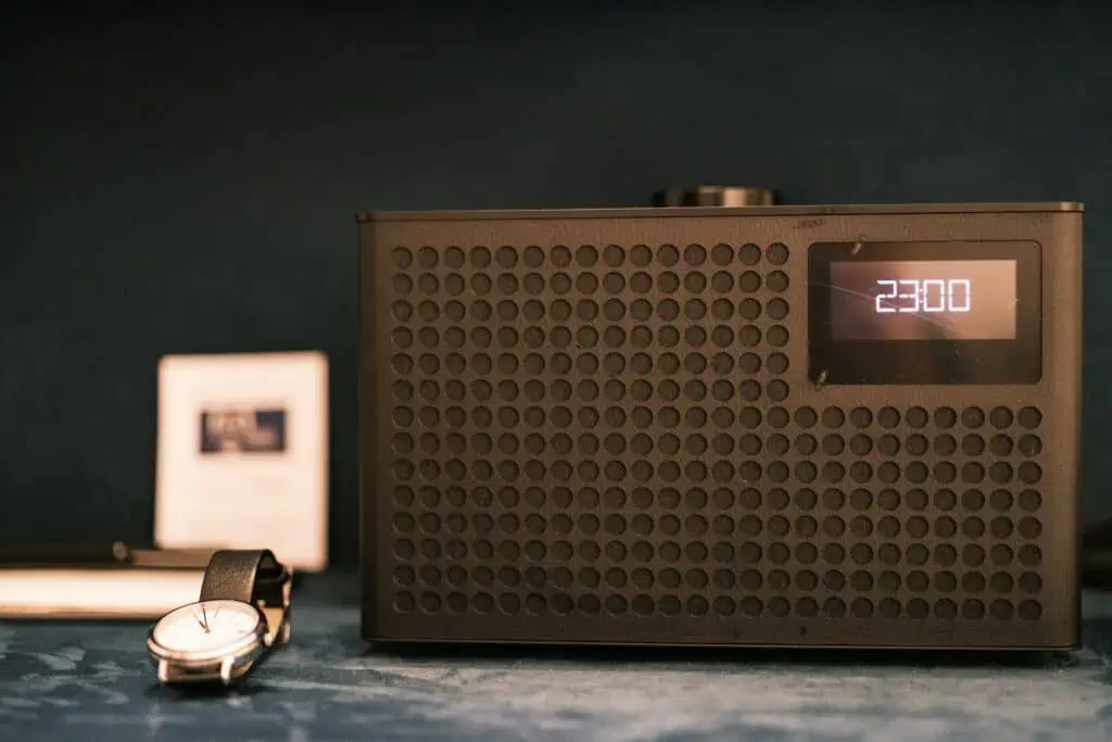 Een wekkerradio naast een horloge op een nachtkastje.