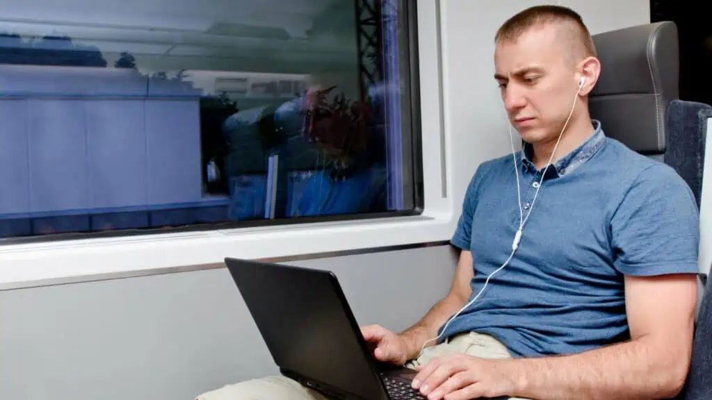 Man in blauwe polo werkt op laptop in een trein