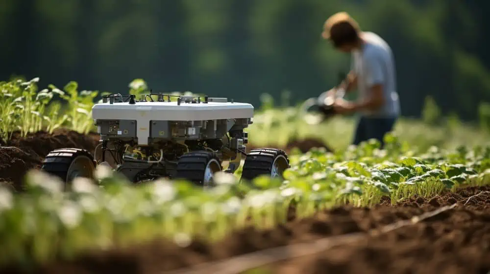 Een kleine robot rijdt door een veld met een werkende boer op de achtergrond