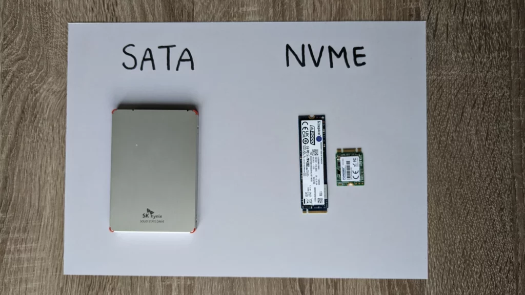Een foto van een SATA ssd (links) en twee NVME SSD's, (rechts, een lange en een korte). Ze liggen op een papiertje en de namen van de type SSD'S (SATA en NVME) zijn erboven geschreven met stift, in zwarte blokletters.
