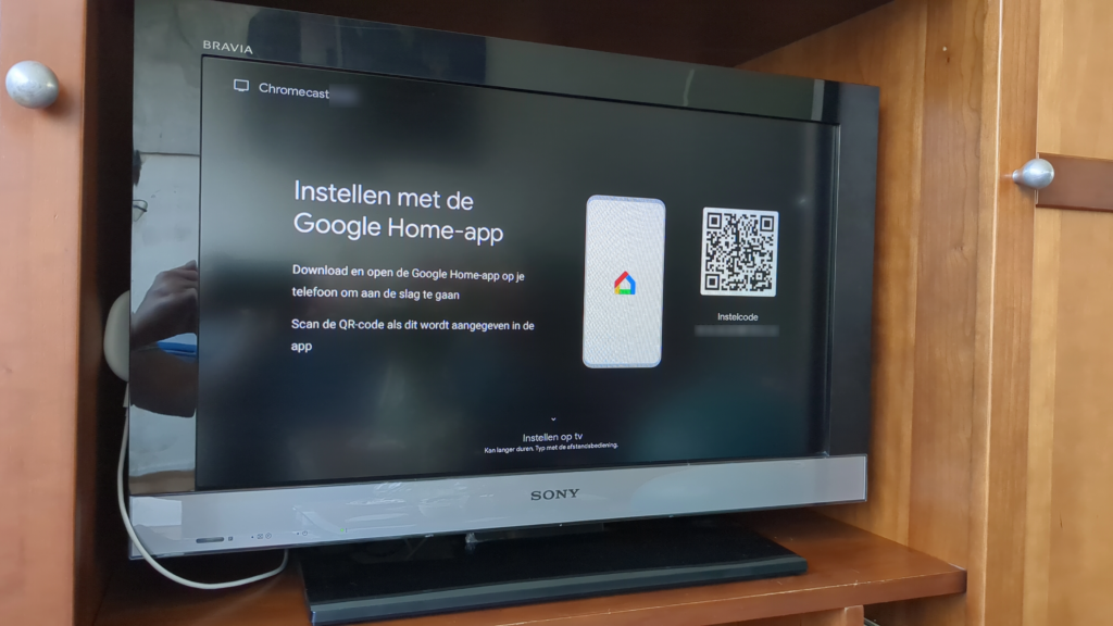 Foto van een tv waarop een QR-code wordt getoond voor het instellen van de Chromecast via de Google Home-app. Onderaan het scherm staat in kleine letters de optie om door te gaan zonder de app te gebruiken.