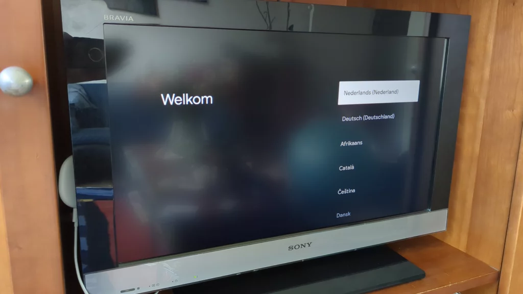 Foto van een tv-scherm met een taalkeuzemenu, geplaatst in een tv-meubel. Op het scherm worden verschillende talen weergegeven om te selecteren via de Chromecast-afstandsbediening.